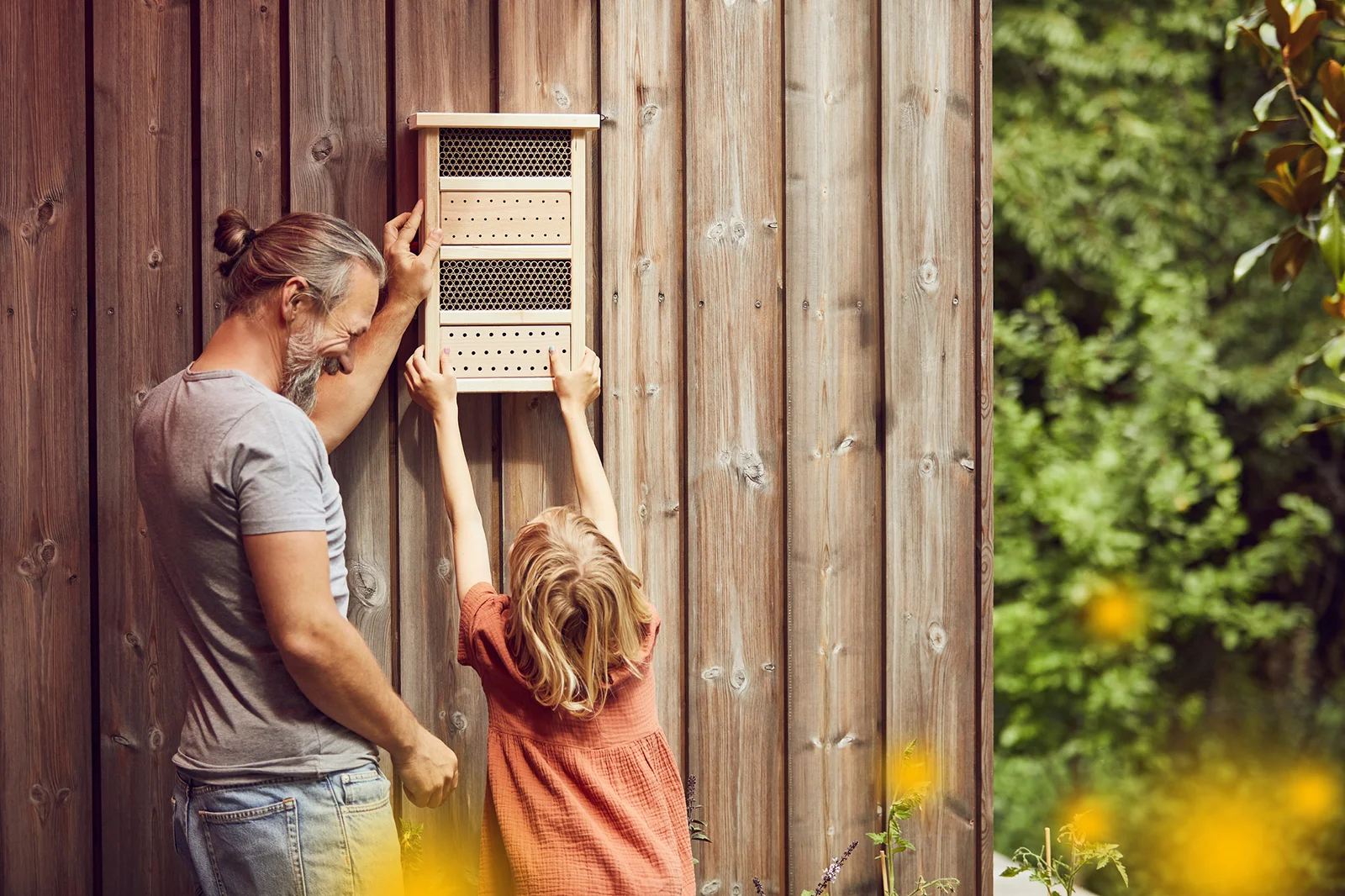 Vater hilft Tochter beim Aufhängen eines Insektenhotels