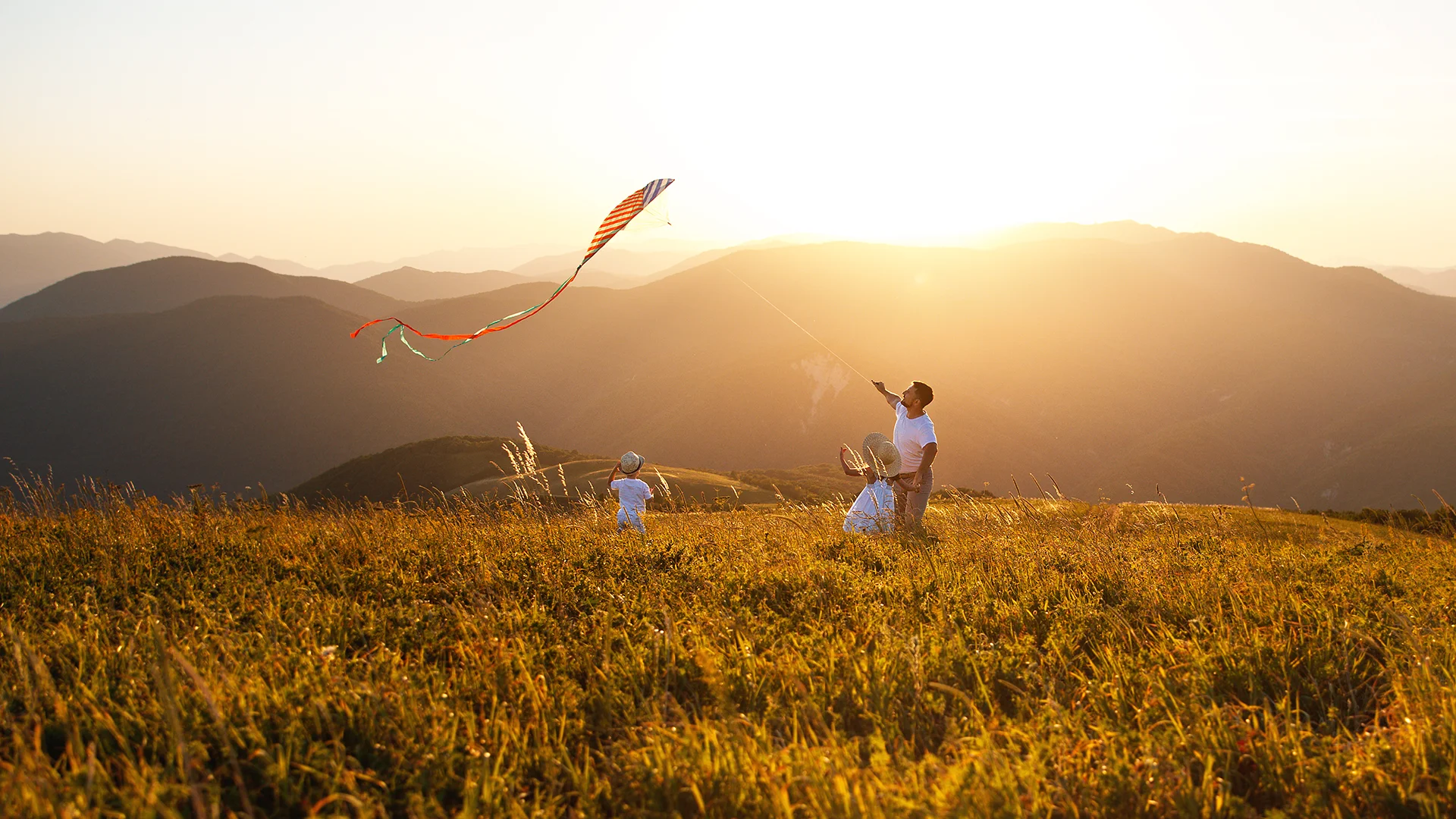 Junge Familie lässt Drachen steigen vor Berglandschaft im Sonnenuntergang