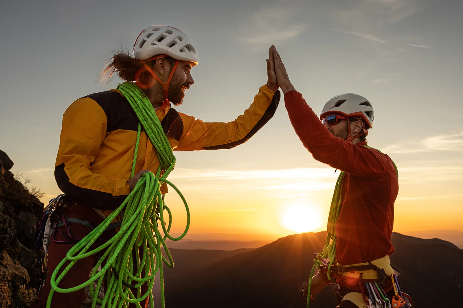 Zwei Bergsteiger schlagen auf Bergspitze vor Sonnenuntergang die Hände zusammen